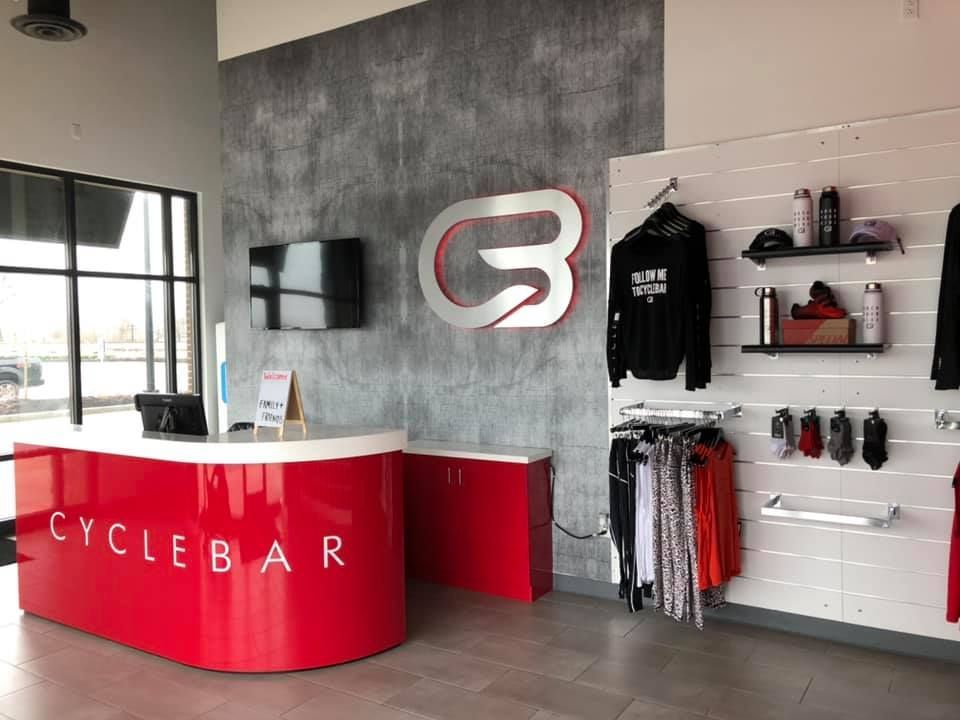 A bright red CycleBar reception desk sits in a modern lobby with a branded logo on a gray, concrete-textured wall.