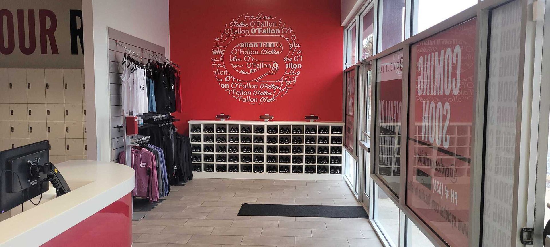 Interior of a clean retail space with a red accent wall featuring white logo decals, hanging apparel, and shoe cubbies.