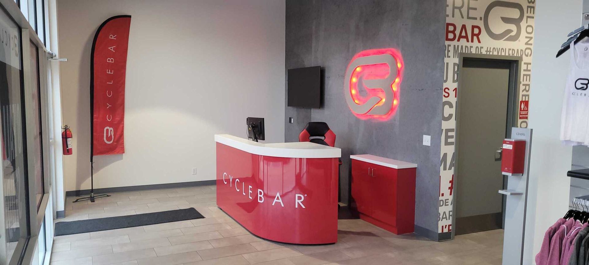 A CycleBar fitness studio interior with a red reception desk, a branded flag, and a gray logo wall.