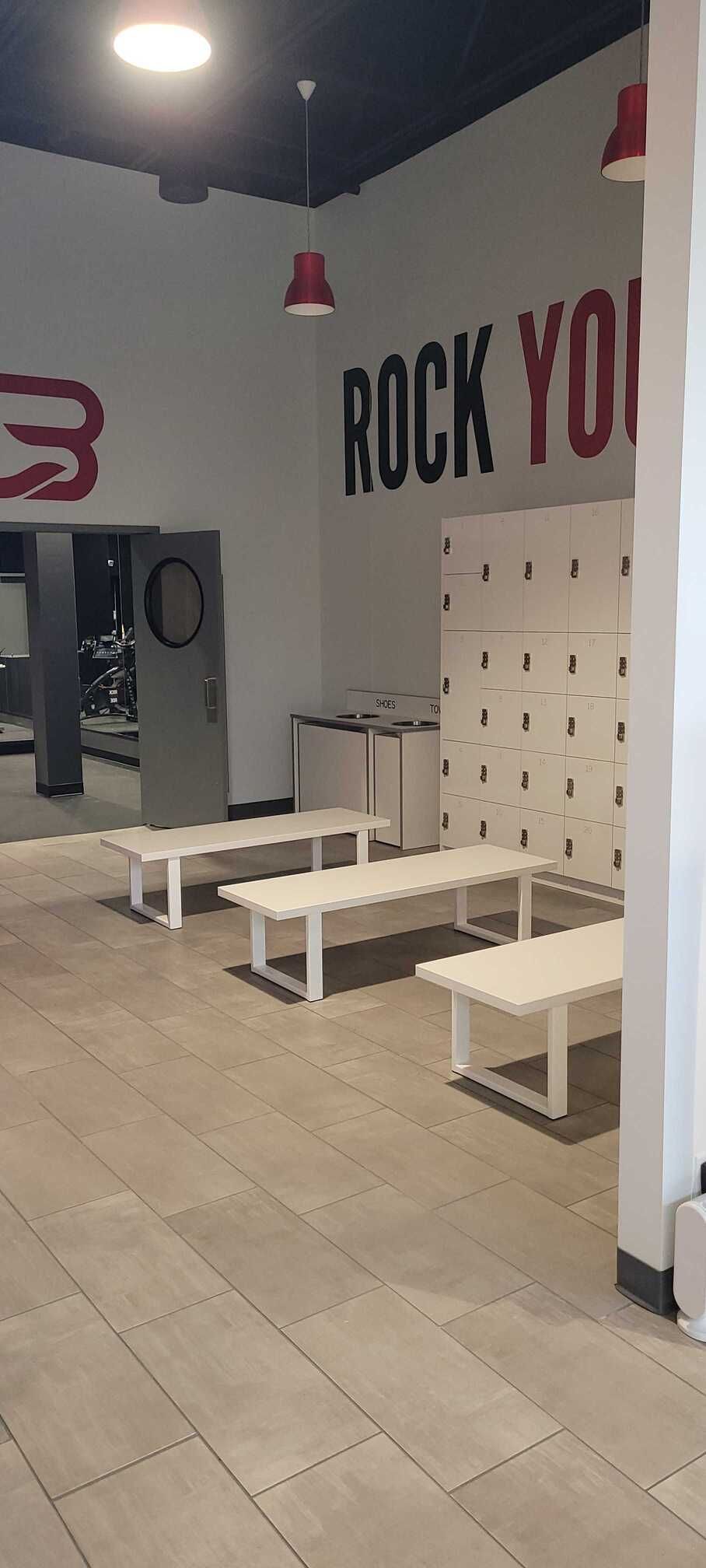 A locker room featuring three white benches, a wall of white lockers, and a red 