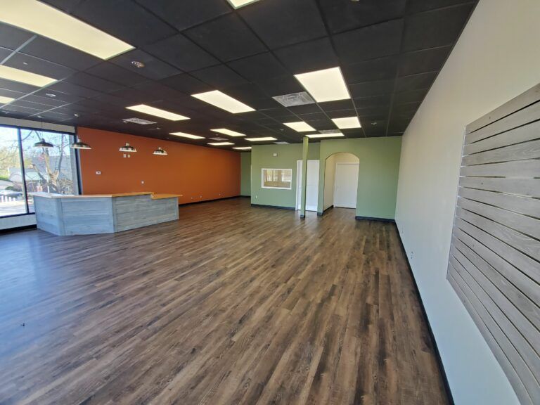 Wide-angle view of a vacant commercial space with wood-look flooring, light-colored walls, and an orange accent wall.