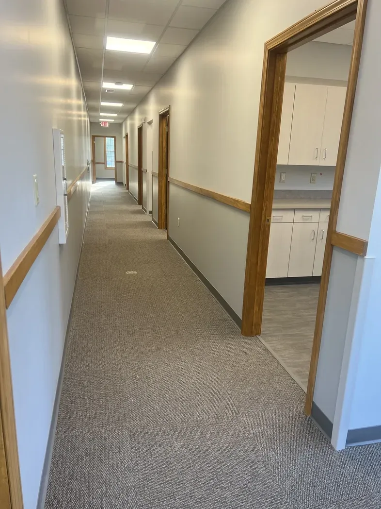 A hallway with patterned carpet and white walls, leading to a doorway on the right showing cabinets in a room.