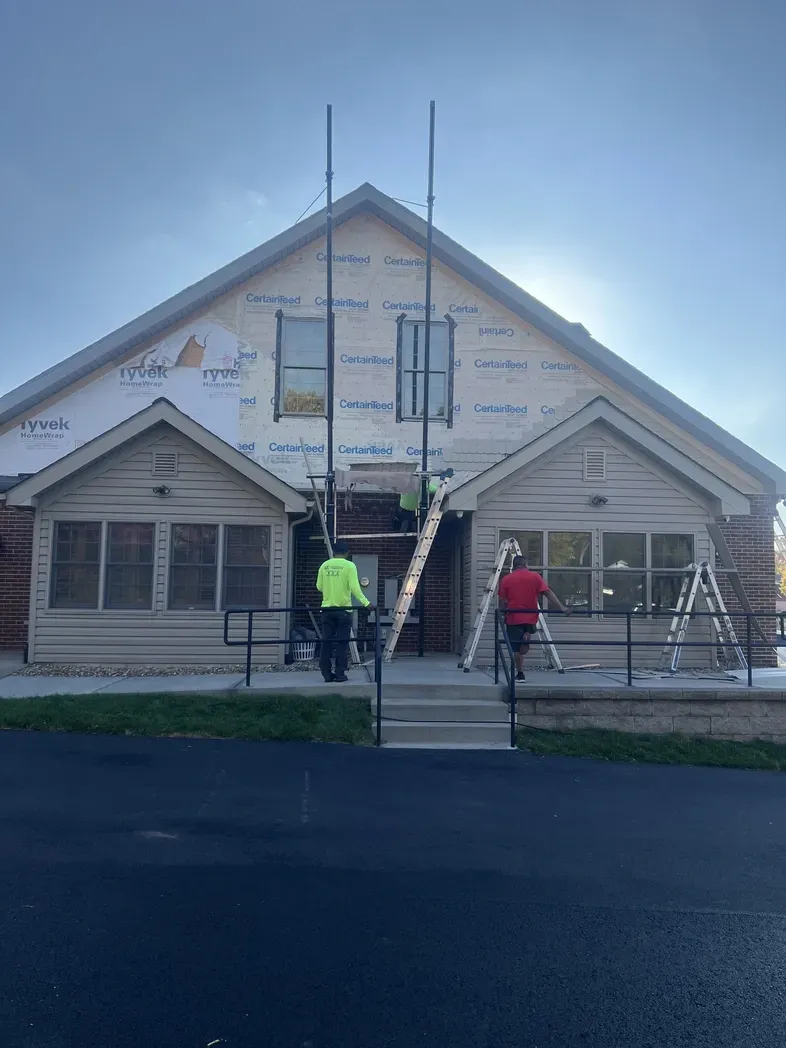 Two construction workers on ladders work on the siding of a building during a renovation project.