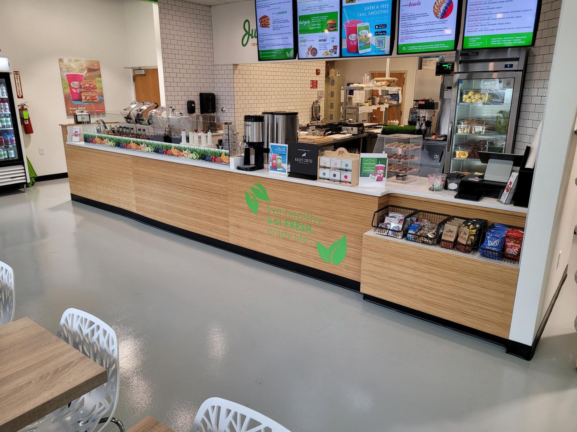 A brightly lit Juice It Up! smoothie and food counter with a light wood-paneled front, digital menu boards, and seating.