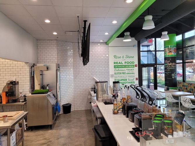 Interior of a modern cafe featuring a white brick wall, a long service counter with appliances, and green accent walls.