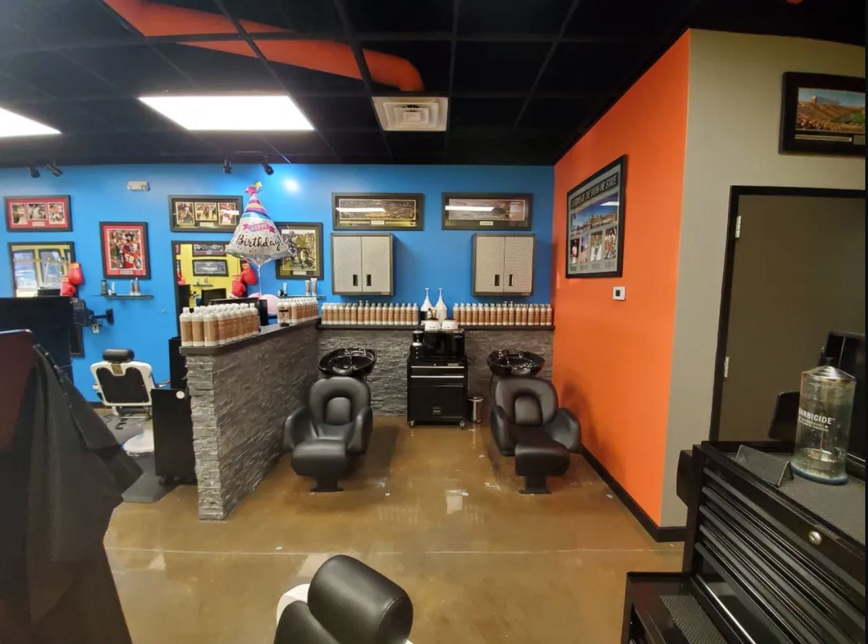 A hair salon with a blue wall, orange accent wall, two shampoo stations, and styling chairs on a polished concrete floor.