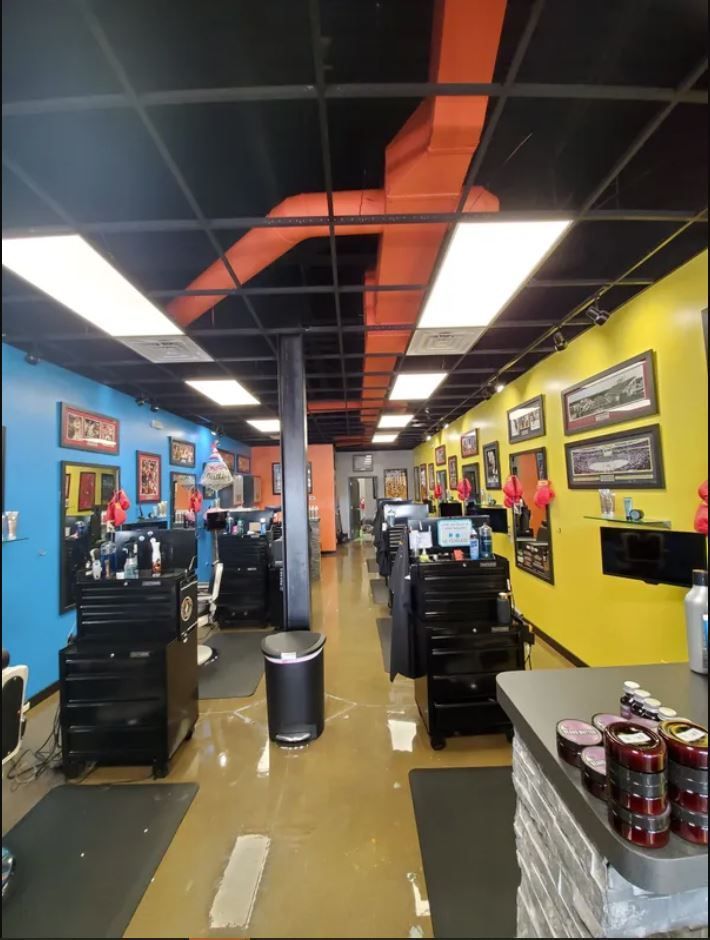 A view down a barber shop aisle featuring a black ceiling with orange ducts, a blue wall, a yellow wall, and stations.