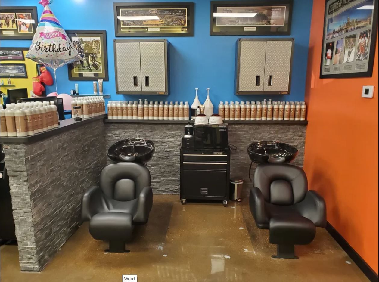 Two shampoo chairs with sinks inside a salon, featuring blue walls, stone-tiled accents, and rows of bottles on shelves.