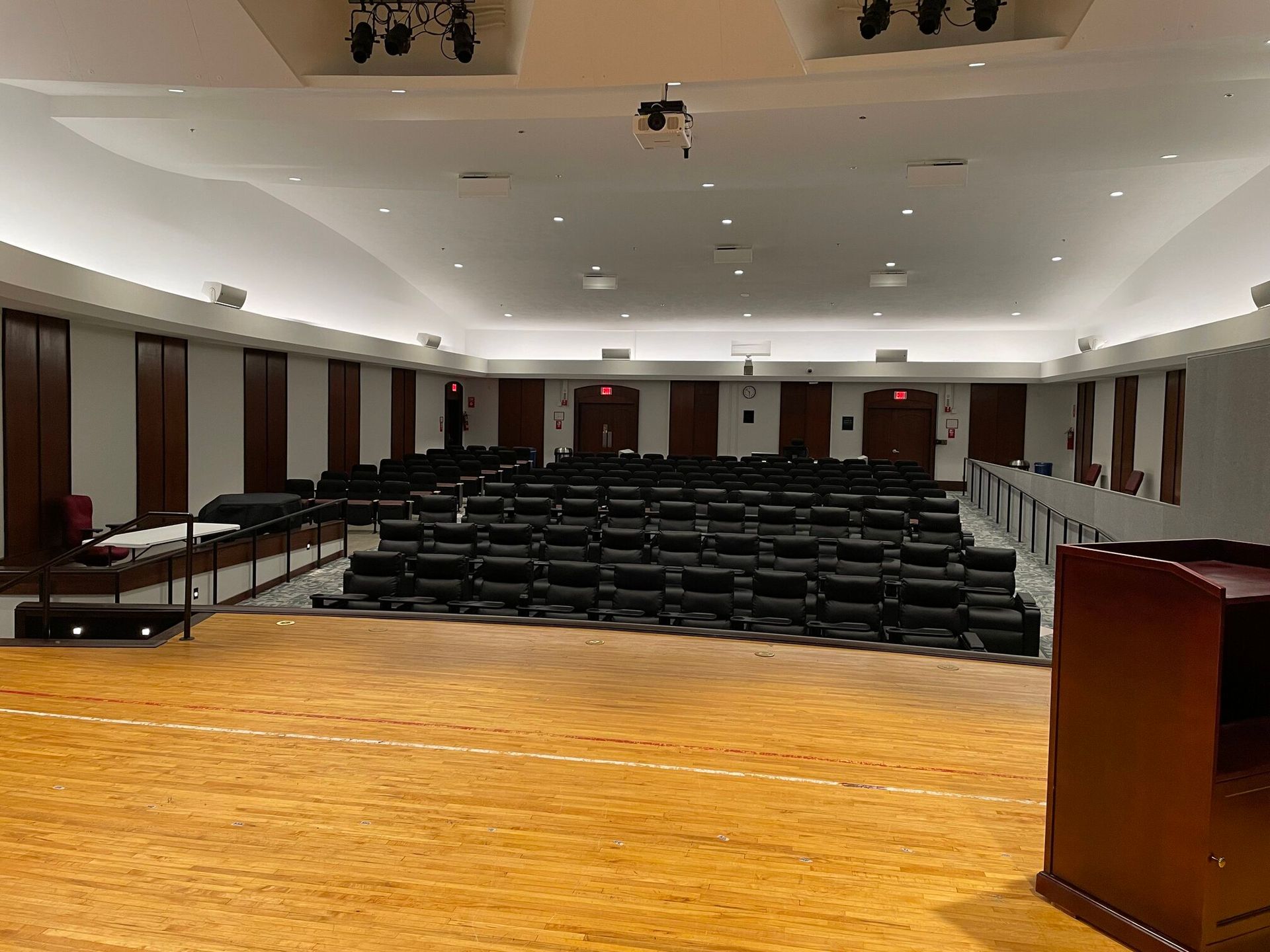Empty auditorium with dark seating facing a wooden stage and a lectern under warm lighting.