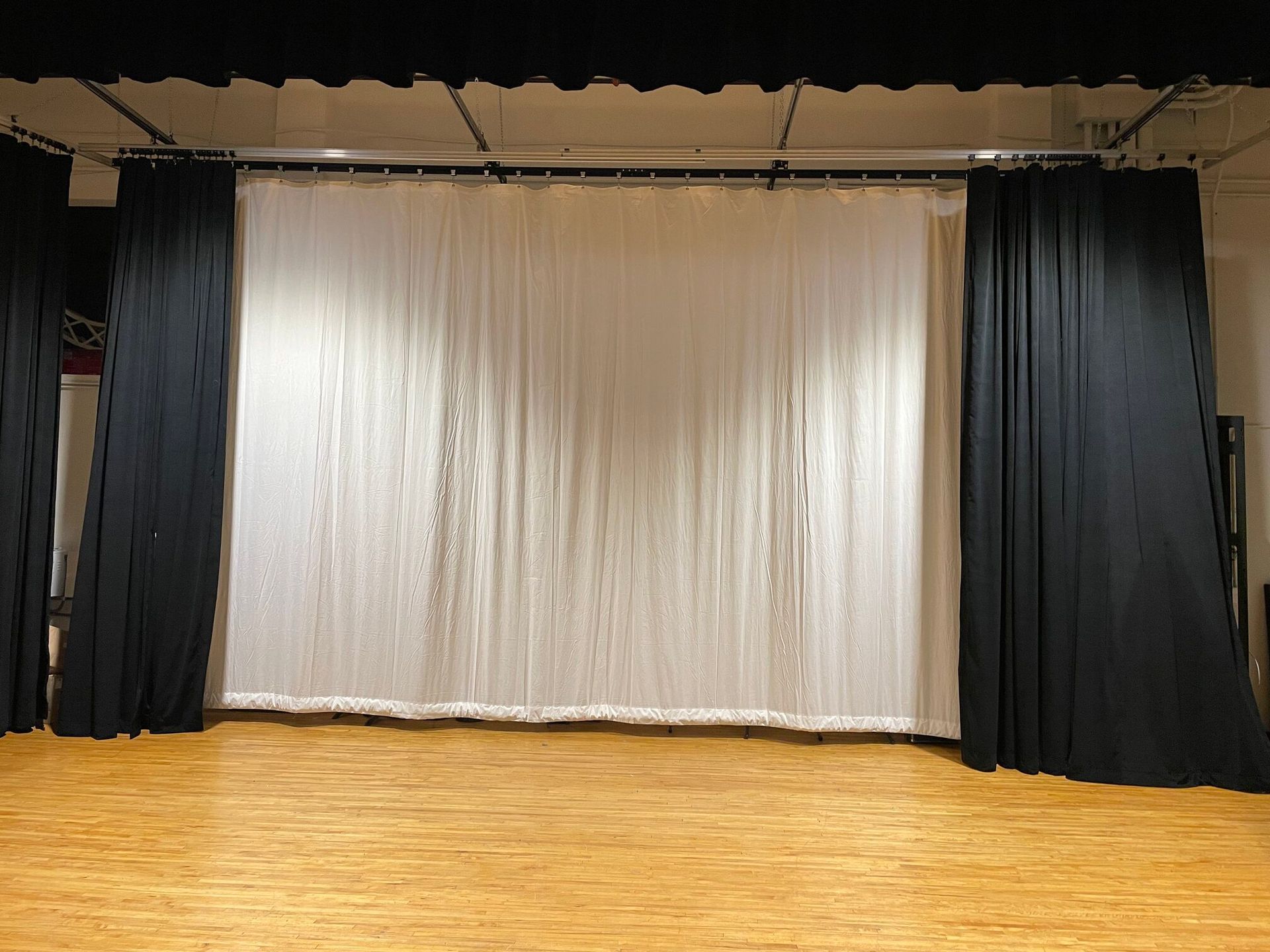 A stage with a white, sequined curtain centered between two black curtains on a wooden floor.