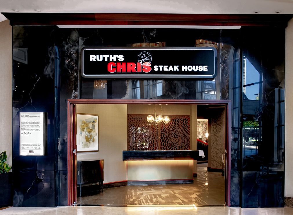The entrance to a Ruth’s Chris Steak House with a black marble facade, white lettering, and an illuminated interior lobby.