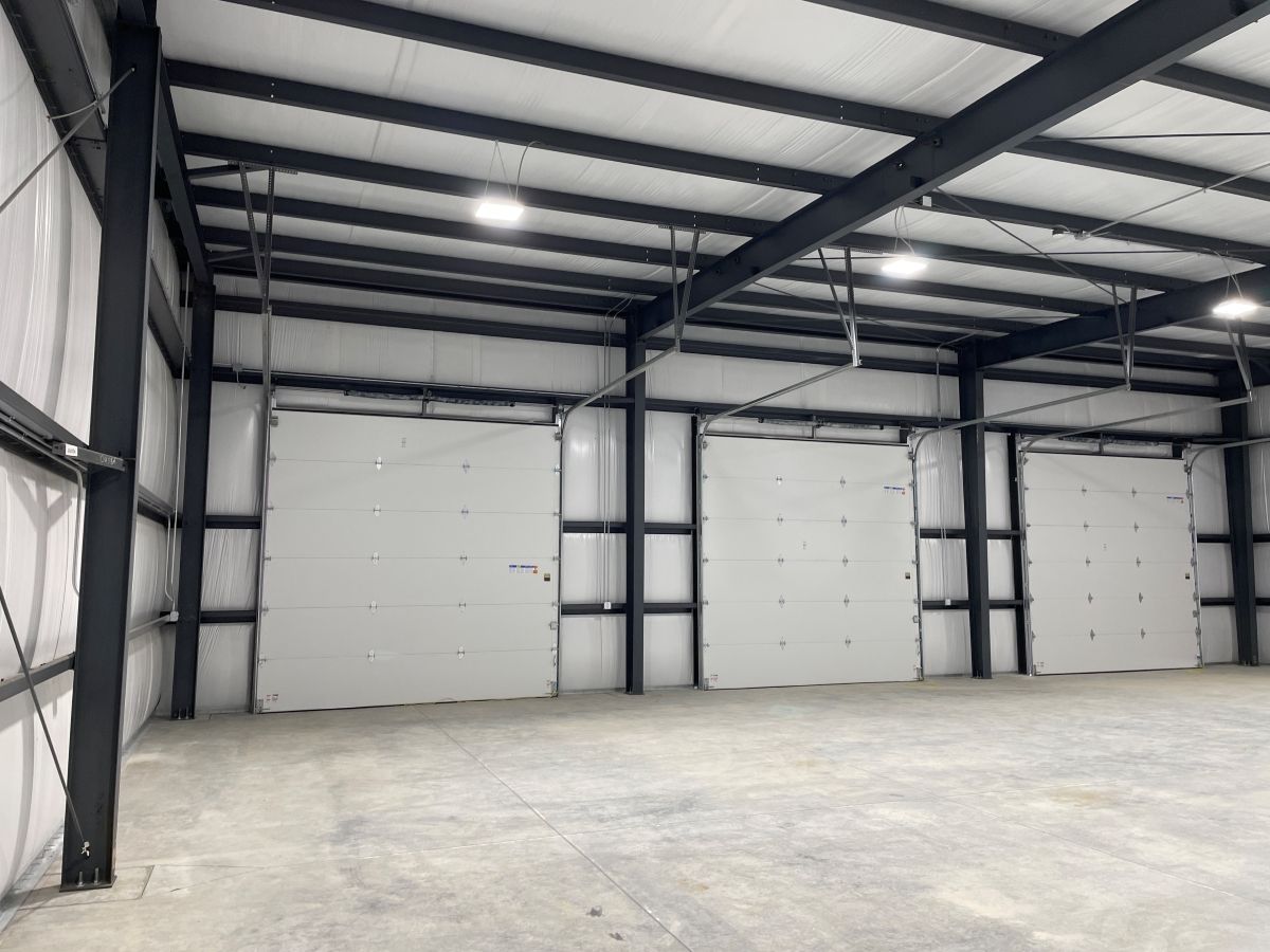 Interior of a large warehouse with a concrete floor, dark metal support beams, white insulated walls, and three bay doors.