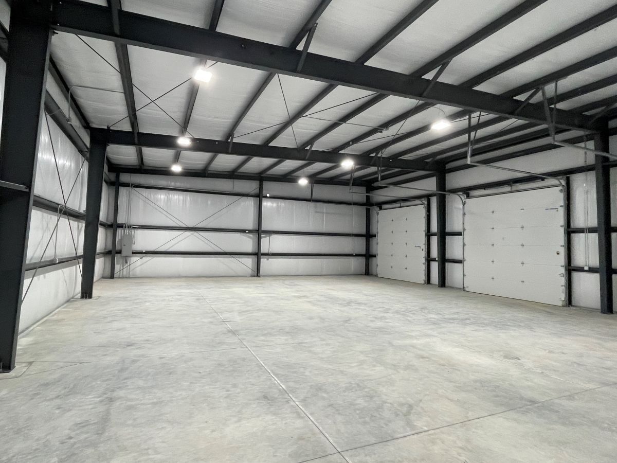 An empty warehouse interior featuring white paneled walls, a gray concrete floor, and black steel support beams.