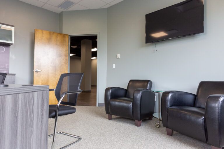 A professional office waiting area with a desk, two black leather chairs, and a television mounted on a gray wall.
