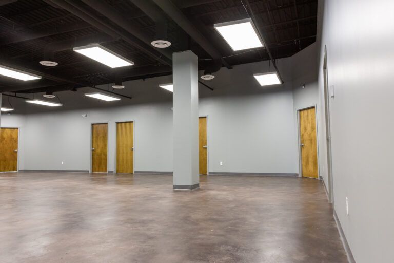 An empty commercial office space with grey walls, brown doors, a central column, and recessed ceiling lights.