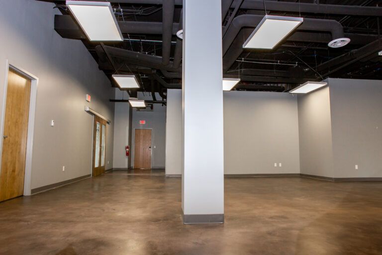 Modern commercial space with concrete floors, gray walls, a central structural pillar, and an exposed dark ceiling.
