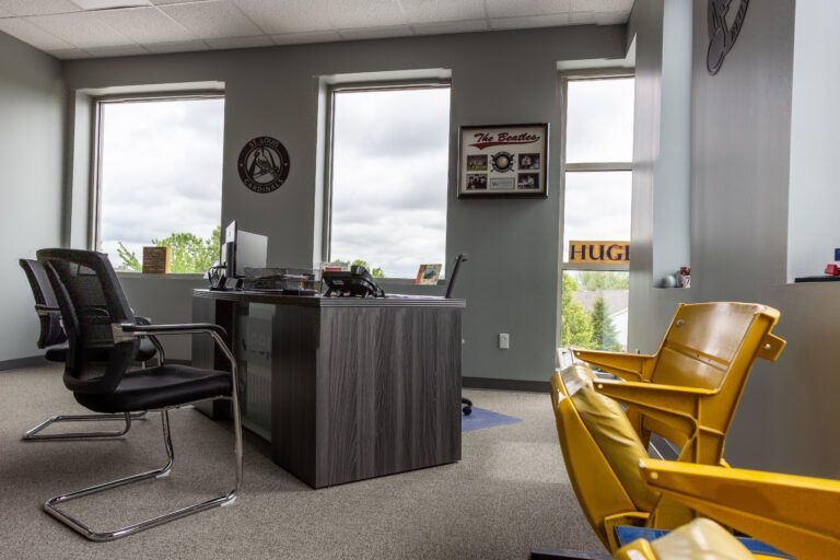A modern home office with a dark desk, two black rolling chairs, and two yellow stadium-style seats in the foreground.