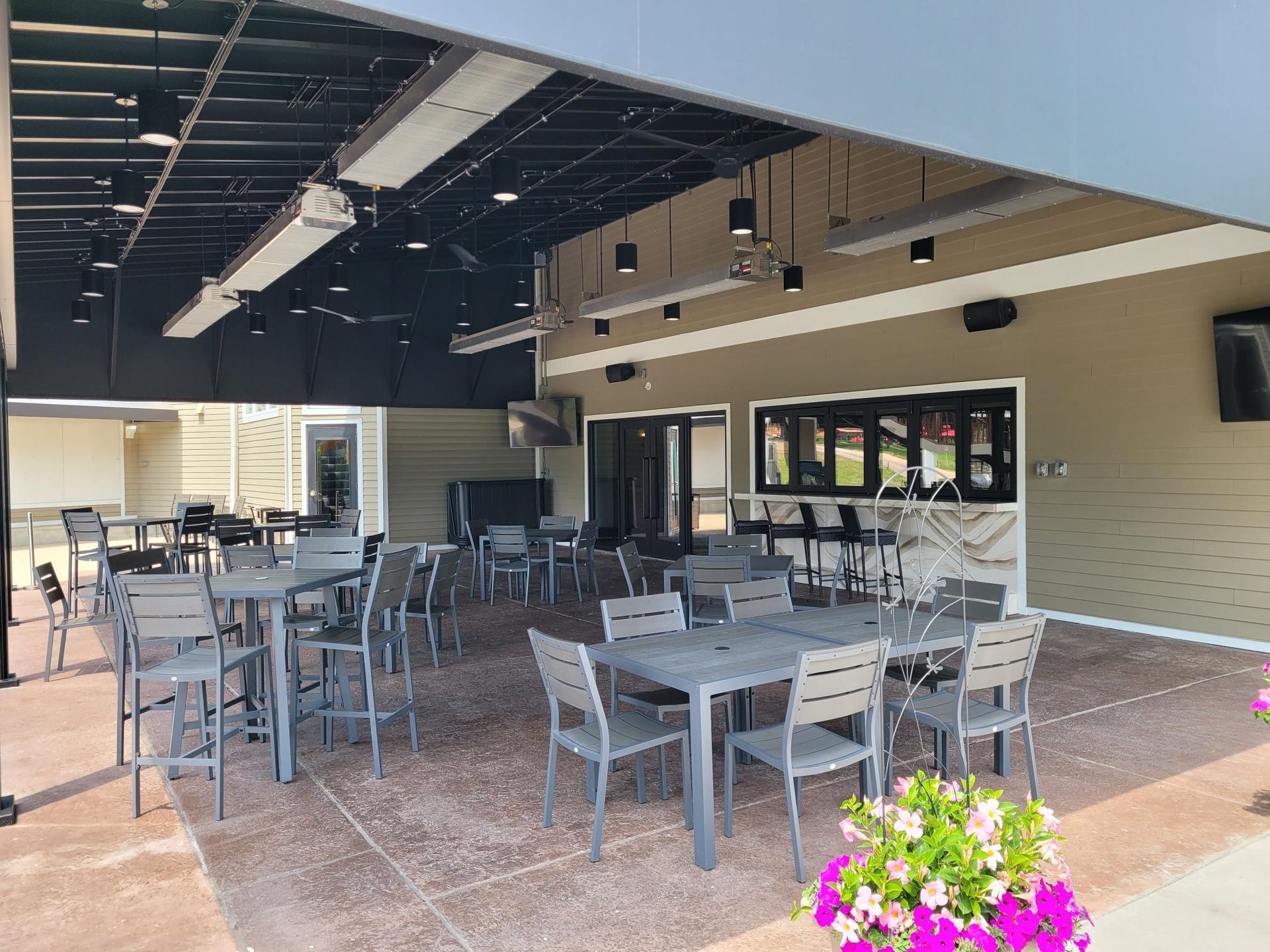An outdoor restaurant patio featuring multiple grey tables and chairs under a dark, covered ceiling with hanging lights.