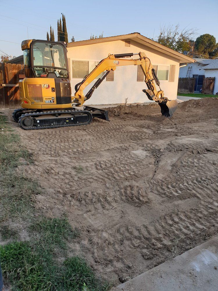 A yellow excavator is digging a hole in front of a house.