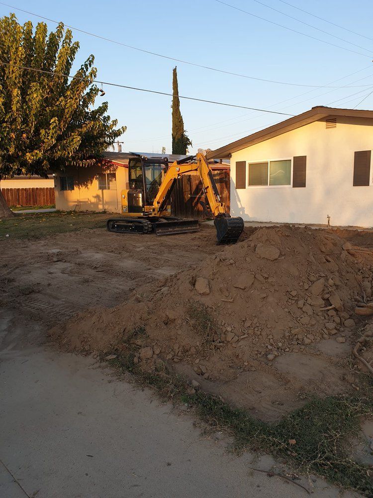 A yellow excavator is sitting in the dirt in front of a house.