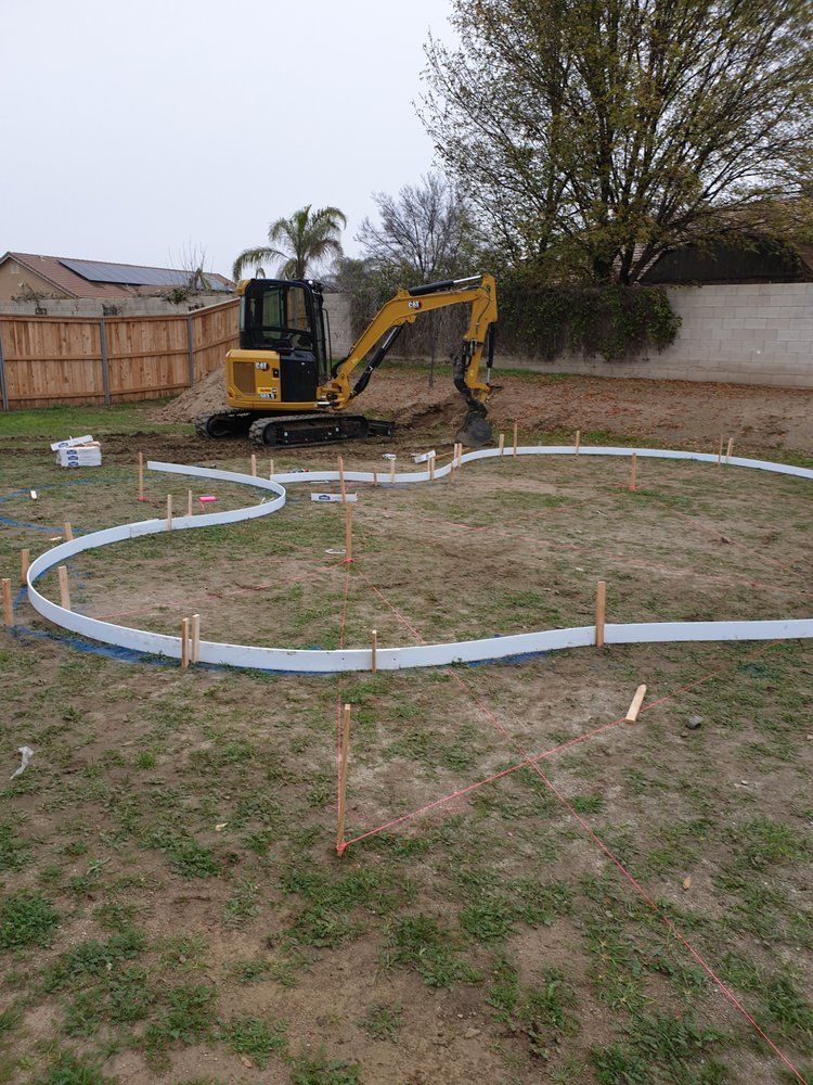 A yellow excavator is digging a hole in a grassy field.