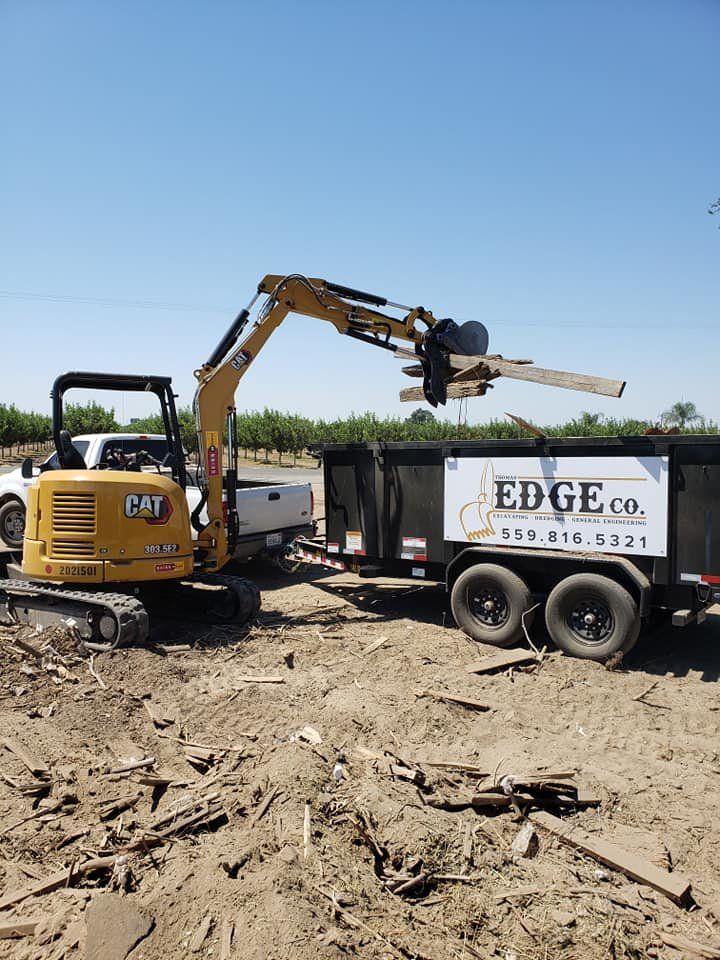 A small excavator is loading a dumpster into a trailer.