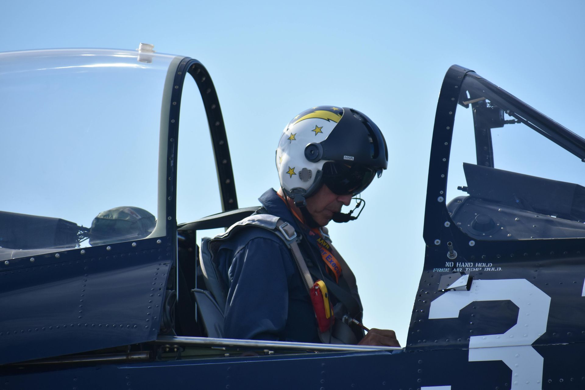 Pilot in helmet and headset in the cockpit of a blue and white plane, preparing for flight.