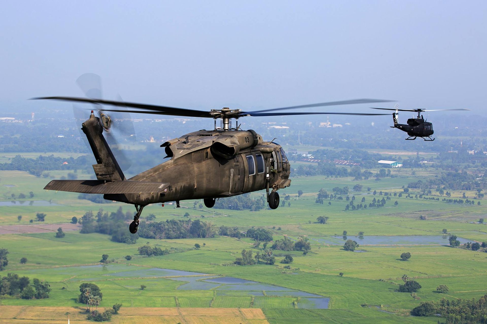 Two Black Hawk helicopters flying over a green field.
