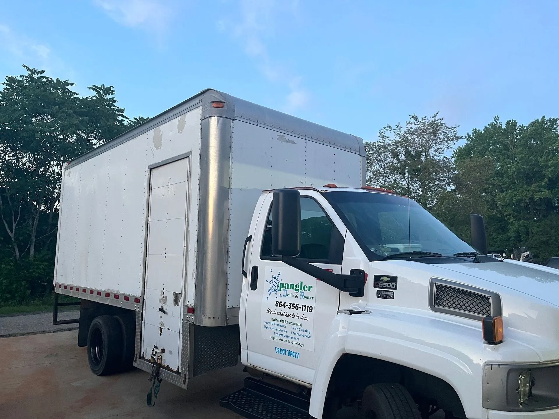 White box truck parked outdoors on a sunny day, shown in side view with trees in the background
