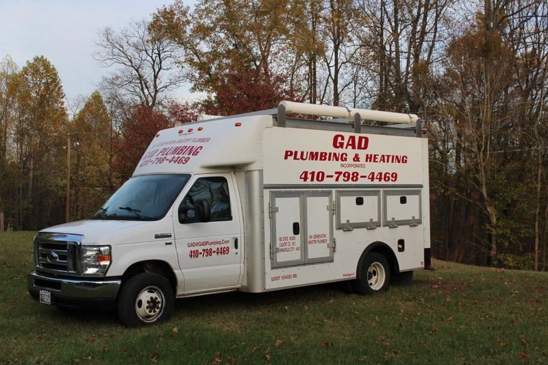White GAD Plumbing & Heating service truck parked on grass with autumn trees behind it