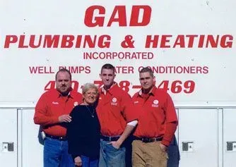 Three men in red shirts standing before a GAD Plumbing & Heating truck sign