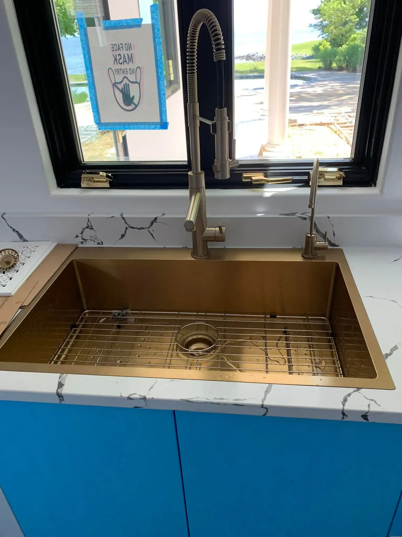 Copper farmhouse sink with black spring faucet on a blue cabinet under a window