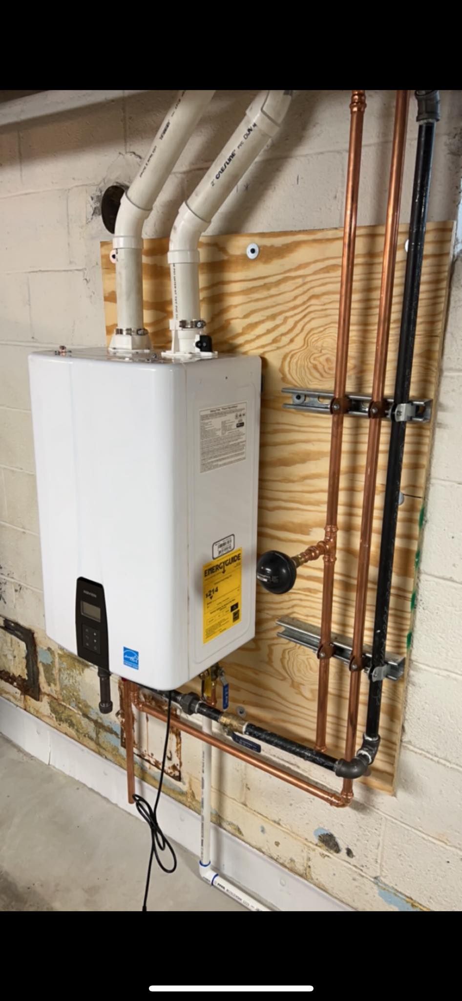 A white water heater is mounted to a wall next to copper pipes.