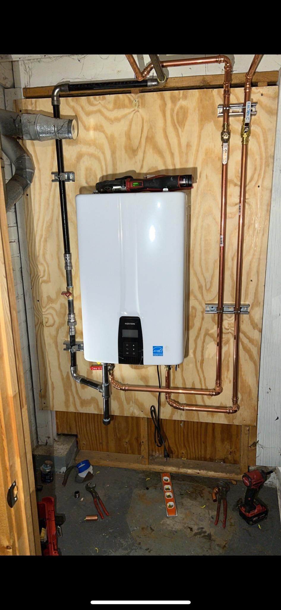 A water heater is being installed in a room with copper pipes.