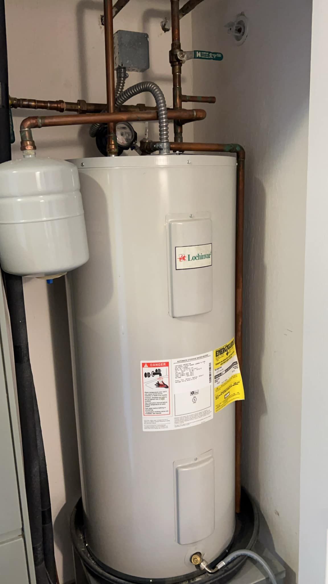 A water heater is sitting in a closet next to a wall.