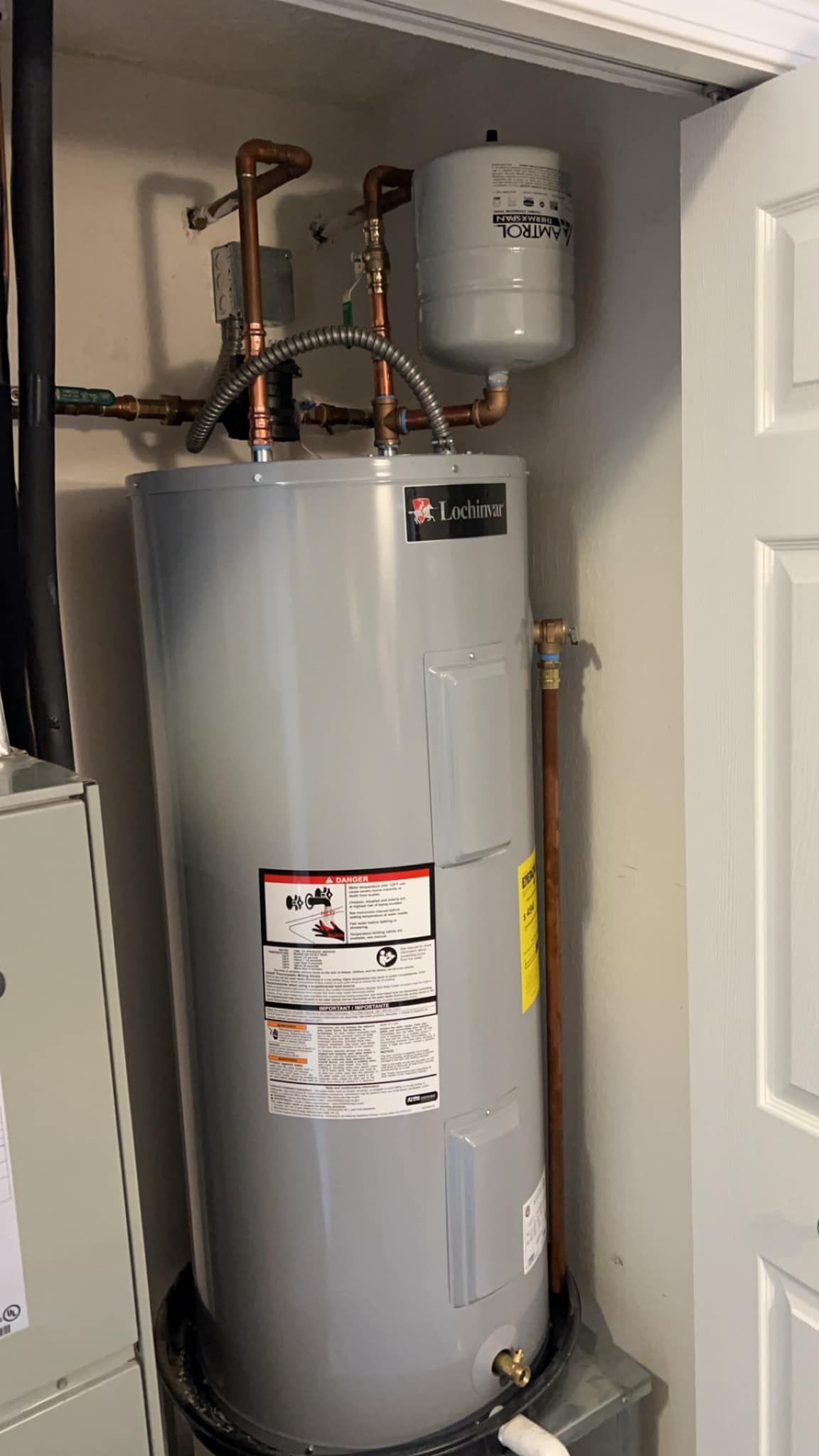 A water heater is sitting in a closet next to a door.