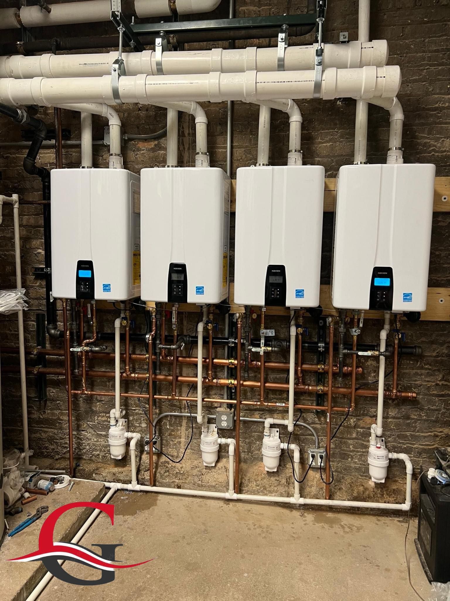 A row of white water heaters are lined up against a brick wall.