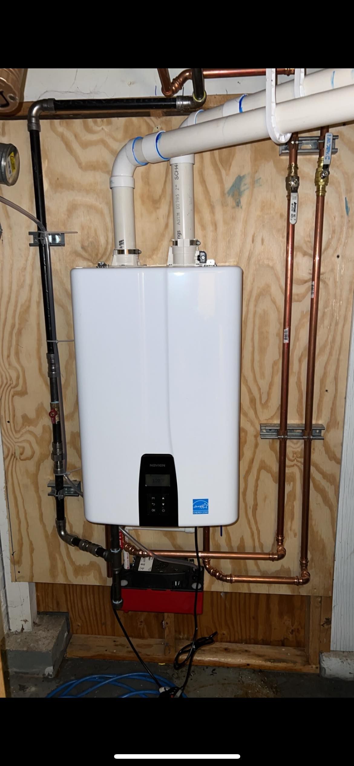 A white water heater is hanging on a wall next to copper pipes.