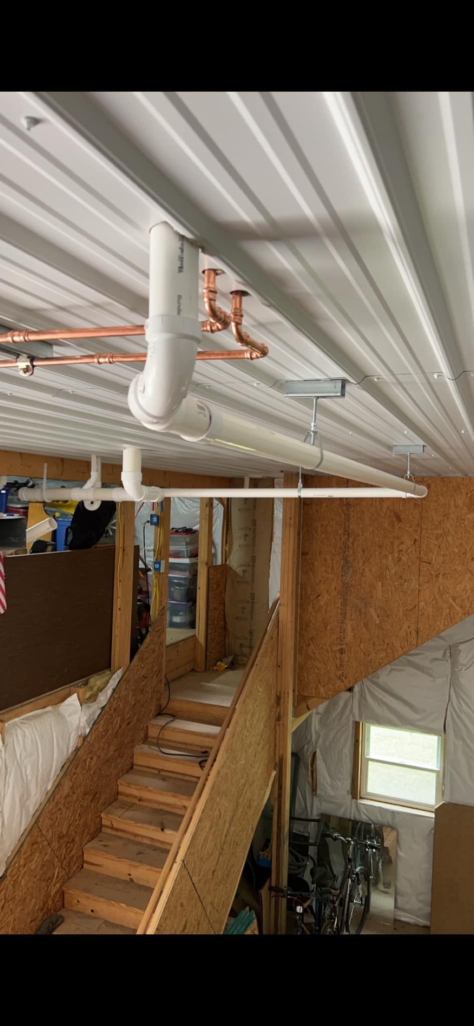A room with stairs and pipes hanging from the ceiling.