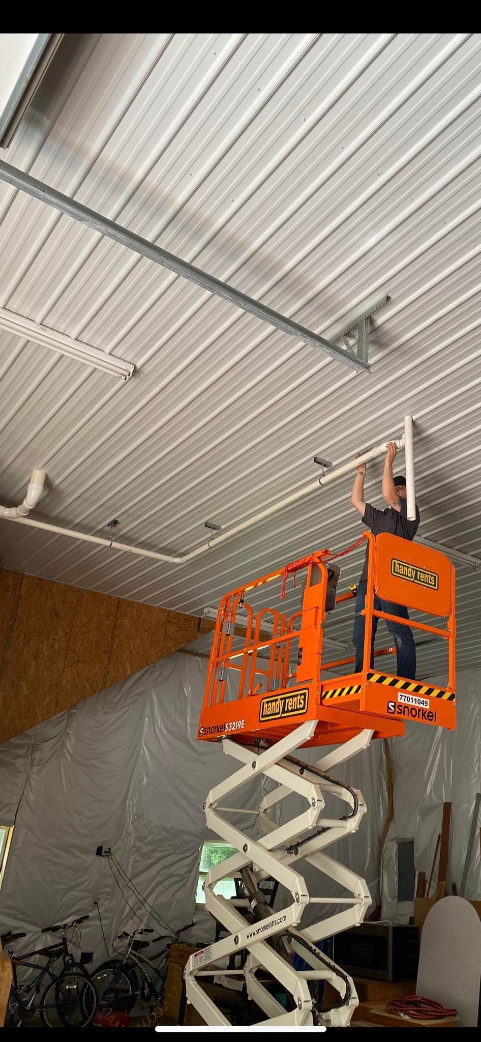 A man is standing on a scissor lift working on the ceiling of a building.