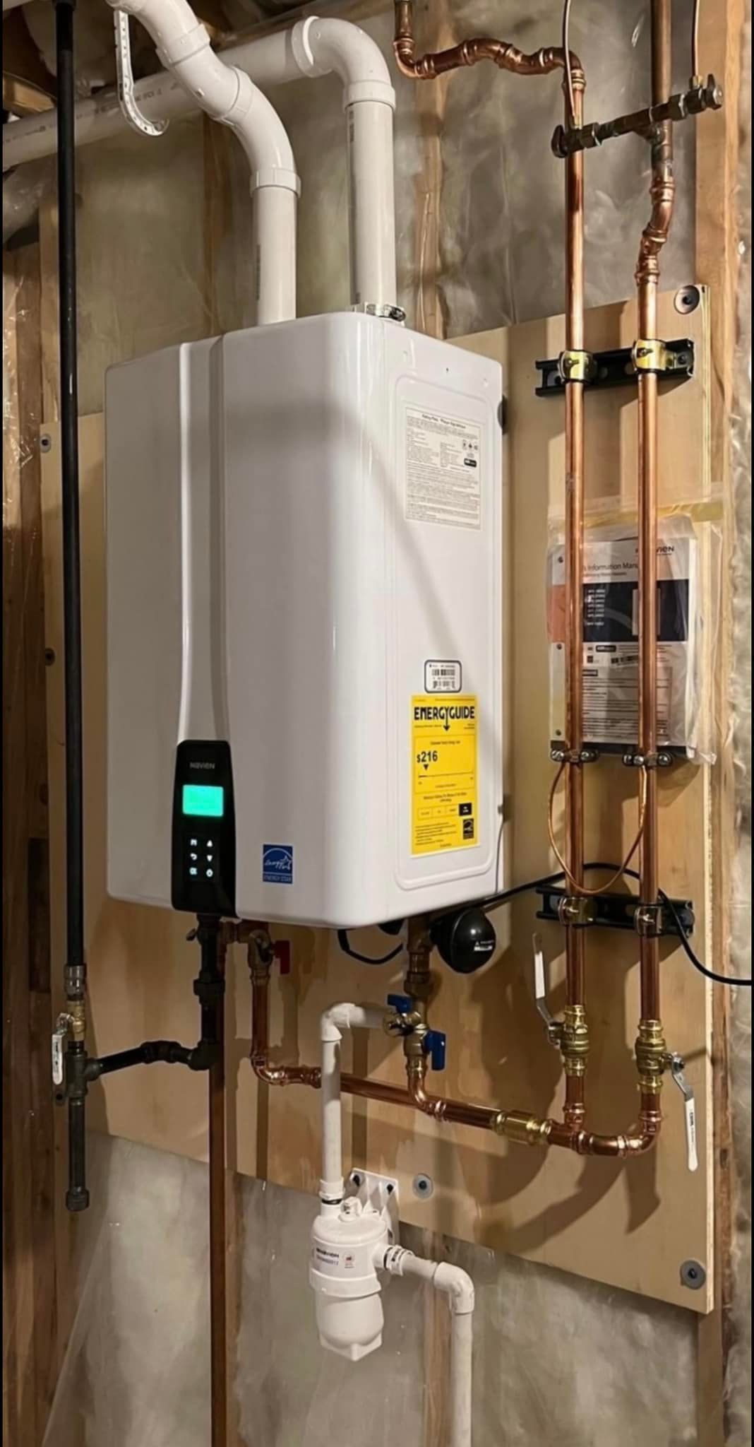 A water heater is installed in a basement next to copper pipes.