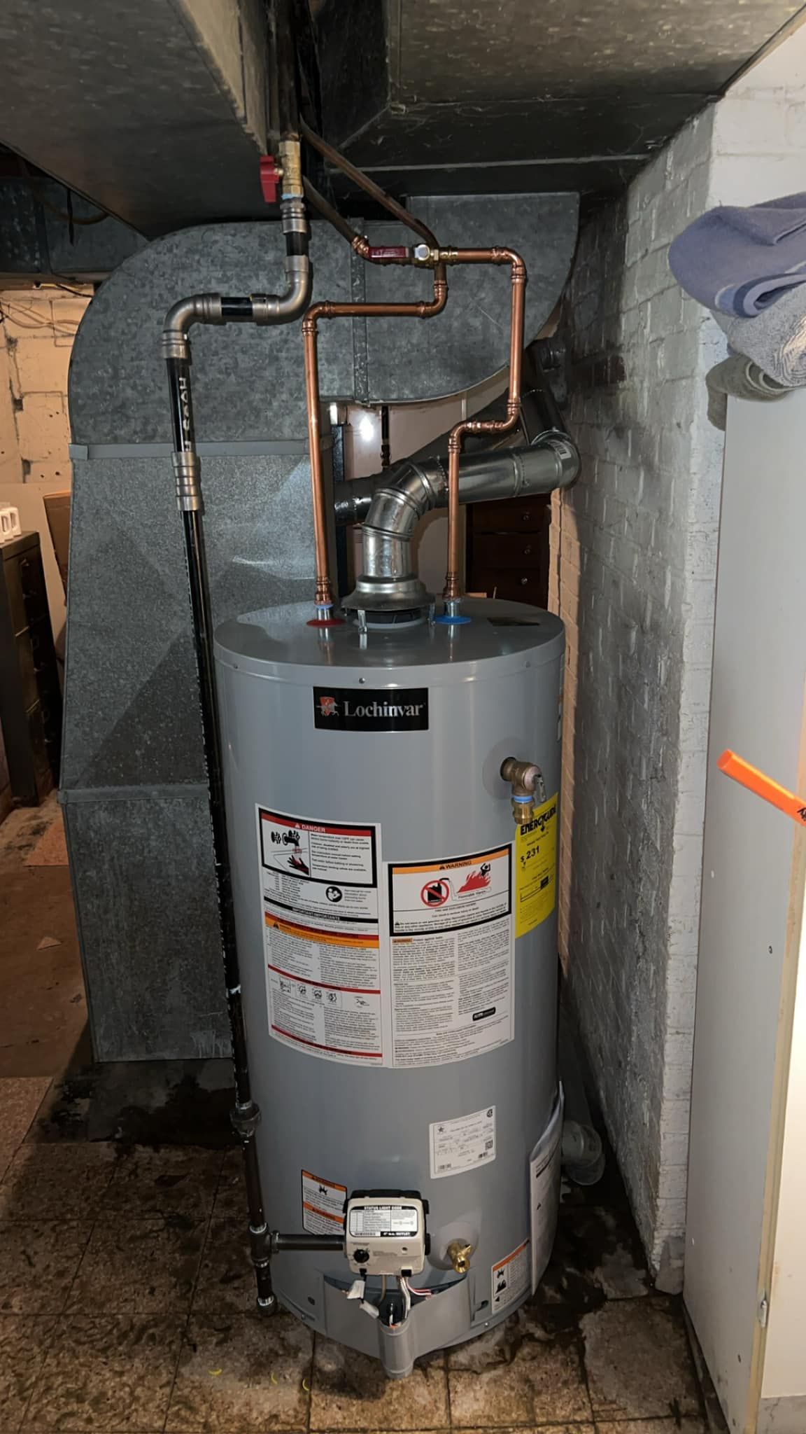 A water heater is sitting in a basement next to a wall.