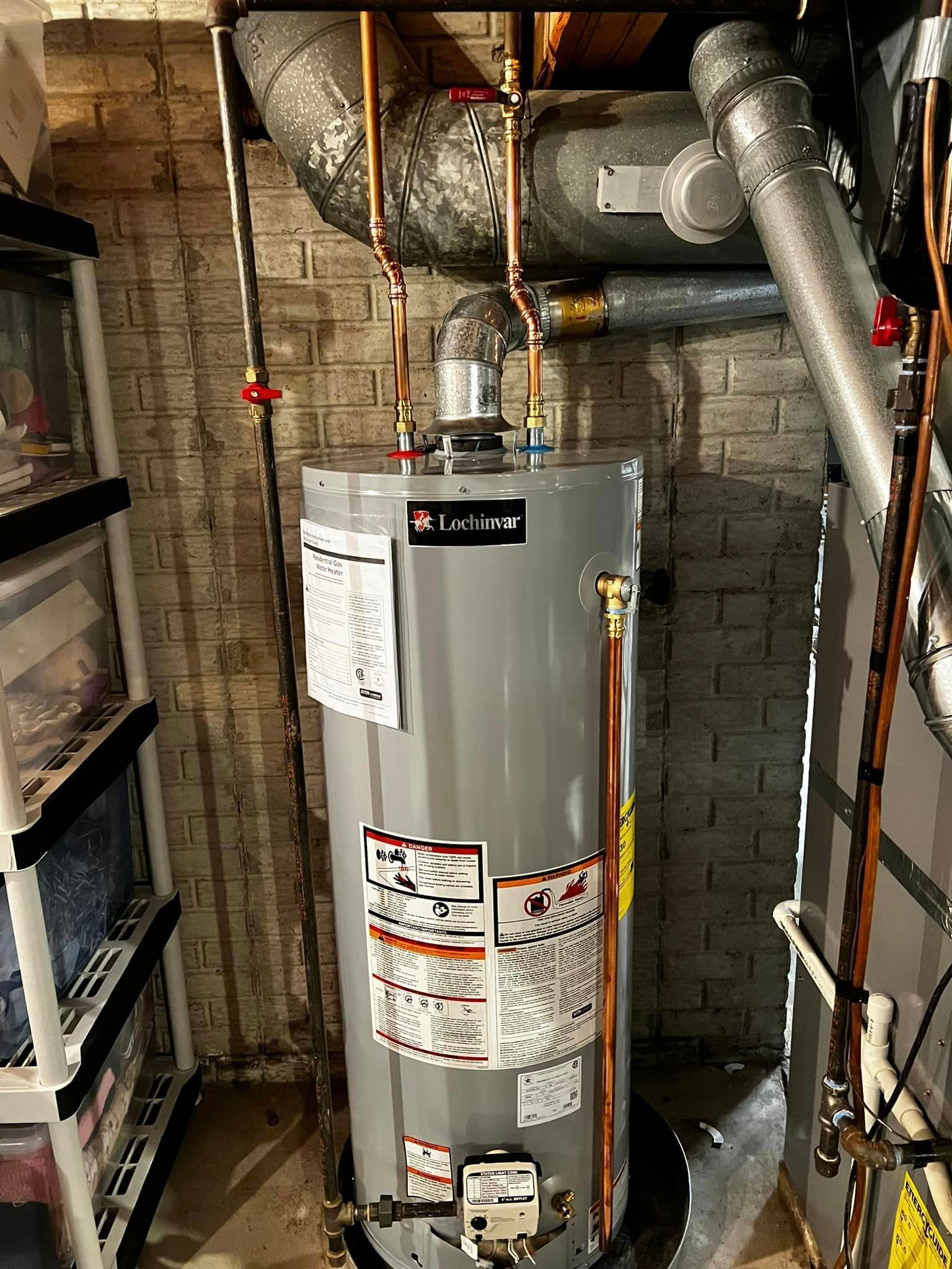 A water heater is sitting in a basement next to a brick wall.