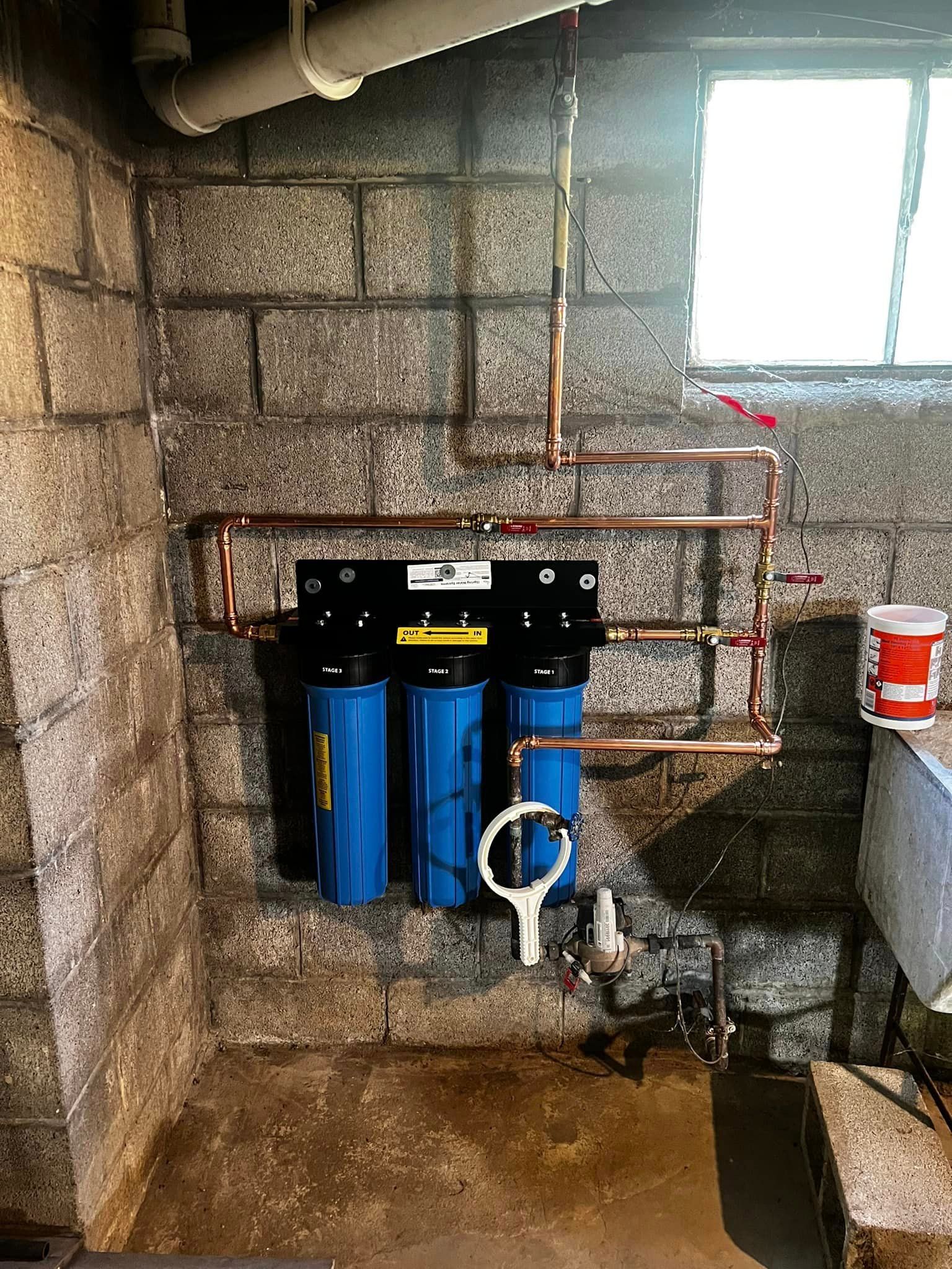 A water filter is installed in a basement next to a window.