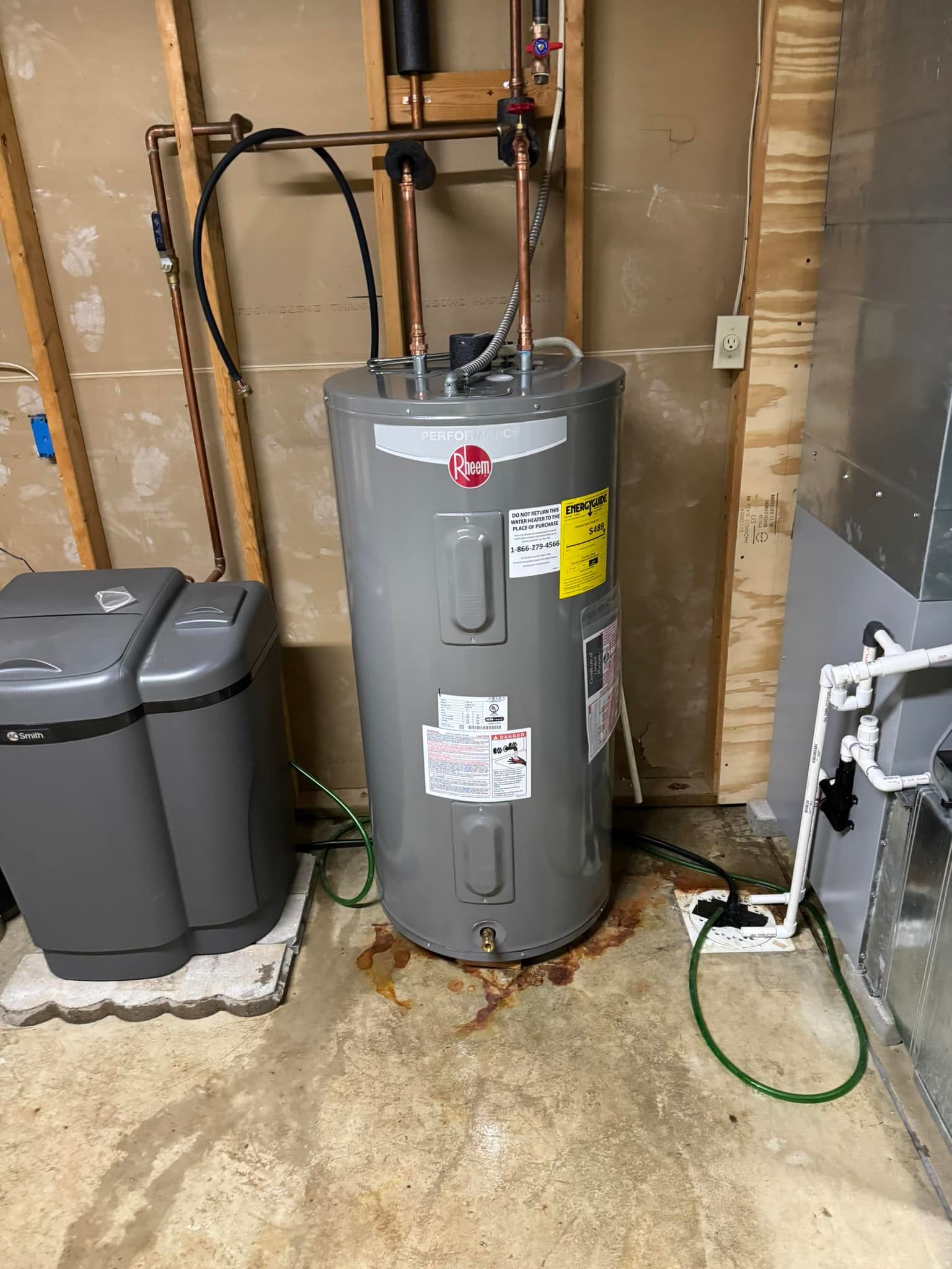 A water heater is sitting in a basement next to a furnace.