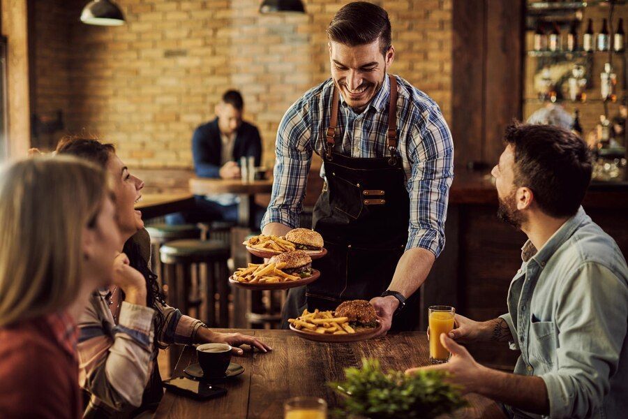 Happy waiter serving food to group of cheerful friends