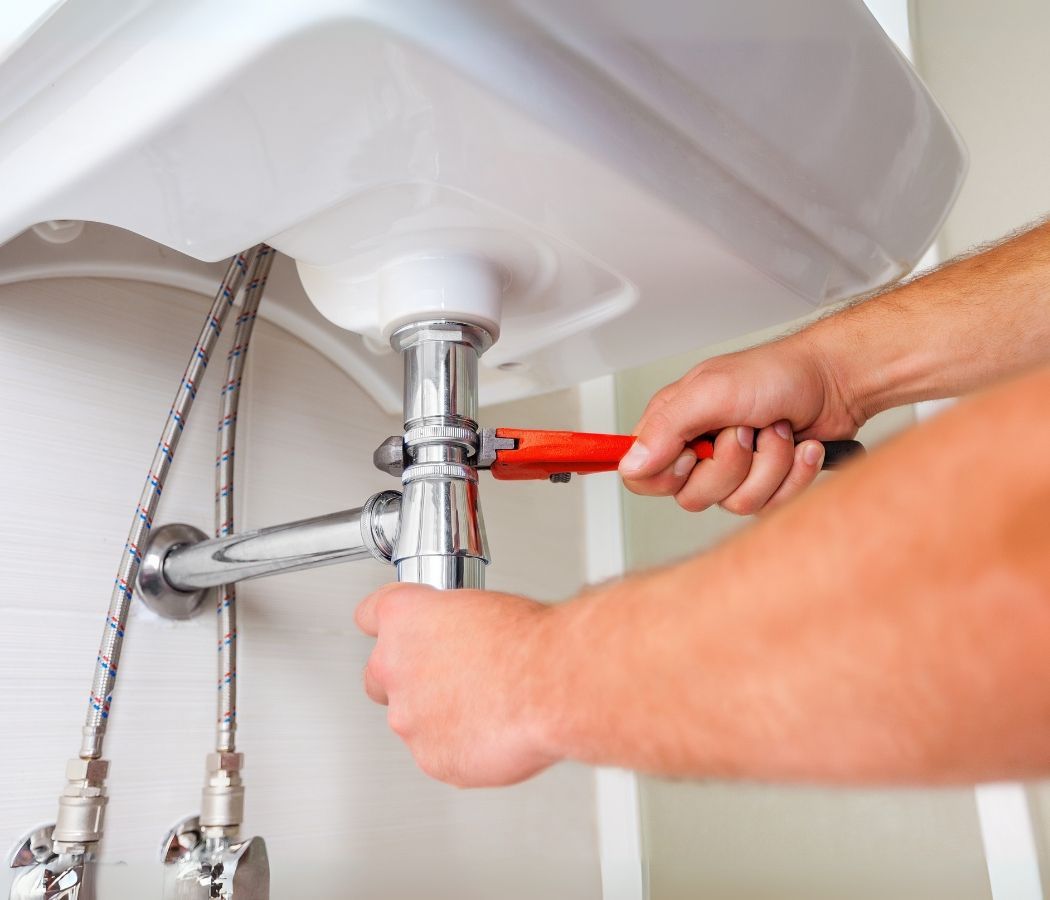 A man is fixing a sink with a wrench.
