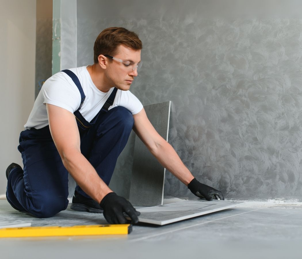 A man is kneeling down while laying tiles on the floor.