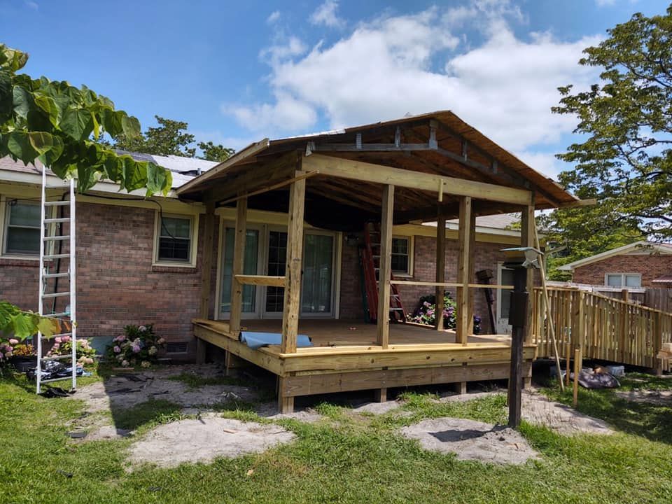 A partially constructed wooden porch addition with a ramp next to a brick house on a sunny day.