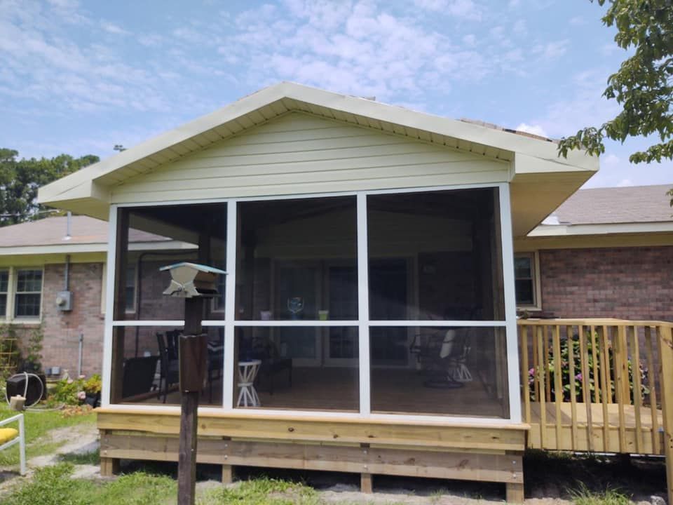 Screened porch addition on a wooden deck, with a beige roof and white trim. Overlooking backyard.